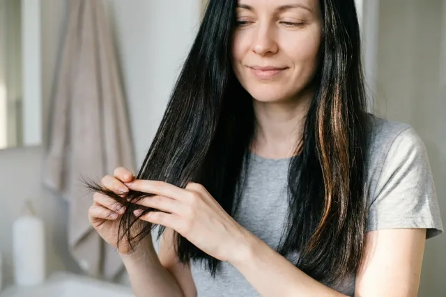 Žena u okna jemně drží suché konečky vlasů po nanesení péče.