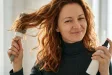 Žena fénuje vlnité vlasy a drží sprej tepelné ochrany.