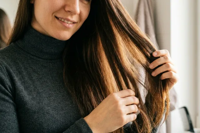 Žena u okna si prsty rozděluje dlouhé tmavé vlasy při domácím testu typu vlasů.